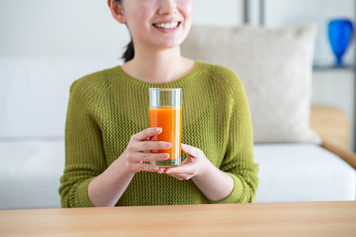 Young Japanese woman drinking vegetable juice in the living room