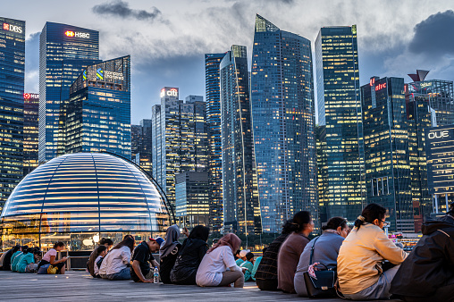 Singapore, 26 January 2024: night falls over Marina Bay, cityscape illuminates with dazzling lights of skyscrapers. Rows of people, tourists, sit in anticipation, they await captivating show