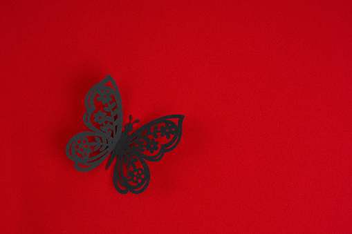 A Black paper butterfly carving on red fabric background. Position with copy space.