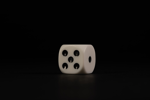 An isolated die with the five and one sides visible on a black background.