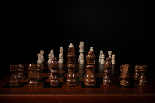 Close up of chess pieces on a chess board.  King, queen, bishop, knight, and rook in the foreground.