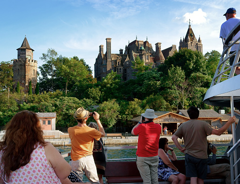 United States, Alexandria Bay - August 22, 2023: Tourists on a Thousand Islands cruise ship taking pictures of Boldt Castle, located on a small island.