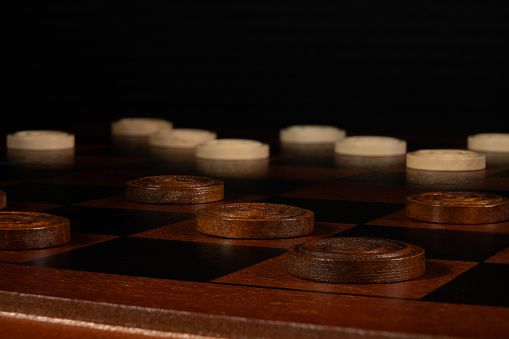 Close up shot of wooden checker pieces on a wooden checker board on a black background.