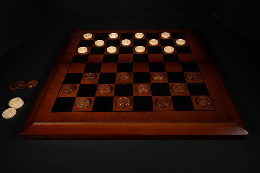 Wooden checker board set up for play on a black background.