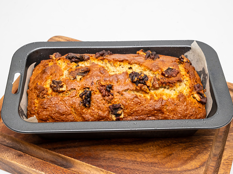 Homemade banana cake with walnut in a dark grey nonstick loaf pan on the wooden board.