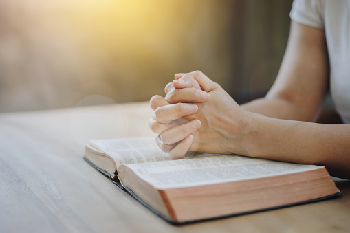 Close up of a woman hands praying on an open bible on a wooden table with window light Bokeh, Christian praise and worship, devotional concept background with copy space. Jesus Christ's disciples life