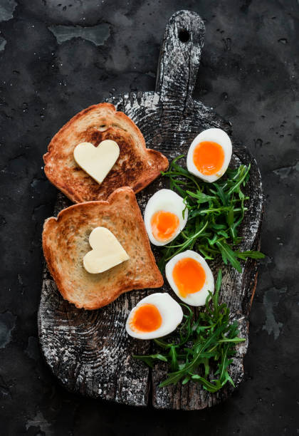 istock Delicious simple breakfast - boiled eggs with soft yolk, arugula, toast with butter on a rustic cutting board on a dark background 1979144854