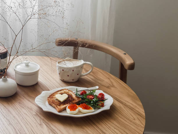 istock Romantic Valentine's Day breakfast, brunch - coffee, toast, eggs with red caviar and salad on a round wooden table 1979144855