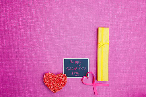 Pink Valentines Day flat lay with chalk board, rice treat, heart ribbon and bright yellow giftbox