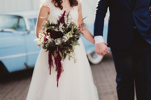 Bride holding bouquet with groom and vintage car