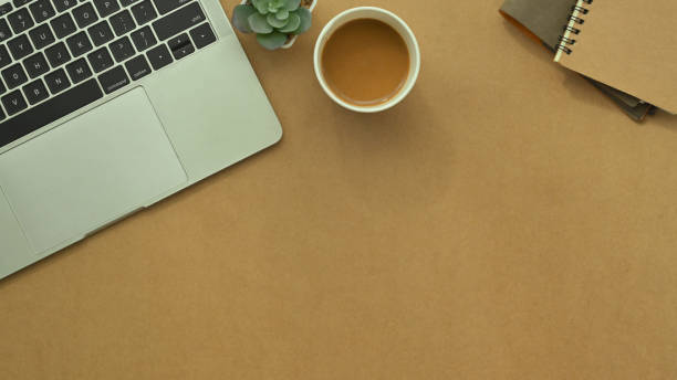 istock Top view laptop, cup of coffee, notepad and plant on brown background with copy space 1979224997
