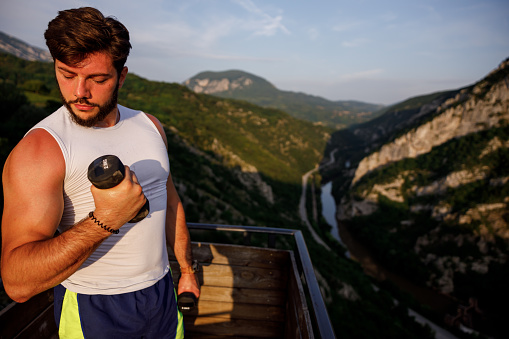 Young handsome muscular man working out on top of a mountain