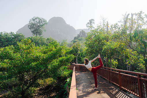 Woman doing yoga on the wooden bridge in the jungles on the background of picturesque mountain