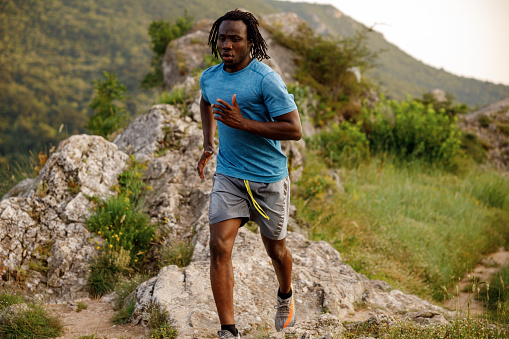 Full length shot of young African man jogging on rocky mountain