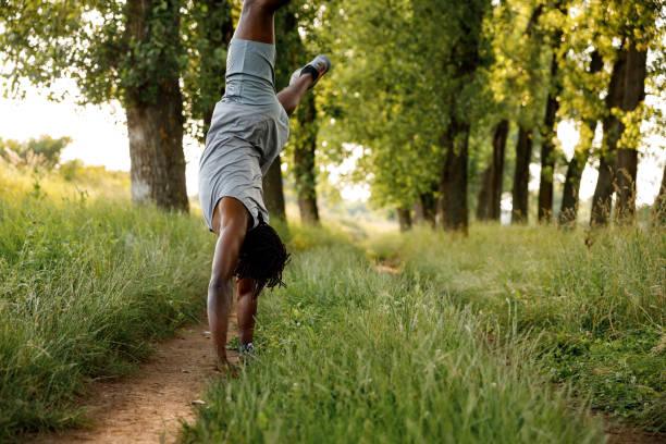 Young African man doing cartwheel exercise in nature on sunny day