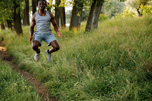 Young African man jumping while exercising in nature on sunny day