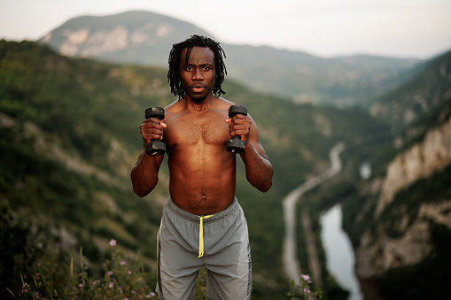 Young African man lifting weights on mountain