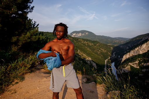 Young African man dressing up blue t-shirt after working out in nature