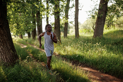 Full length shot of young African man jogging in nature on sunny day