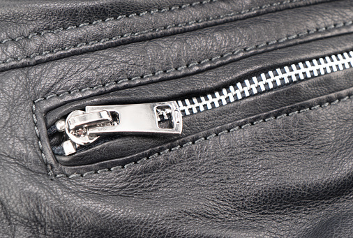 Macro shot of zipper on black leather texture background with stitching. Close-up of black leather material