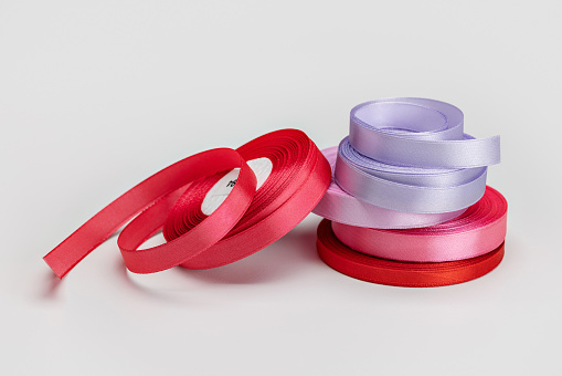 Rolls of bright satin ribbon for sewing and decoration on a light background.