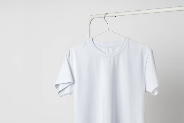 istock Plain white T-shirt hanging on hanger against white wall 1979293393