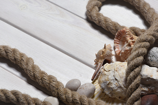 Seashells, mooring rope and pebble stones on the white wooden desk table background top view. Sea travel flat lay concept background with copy space.