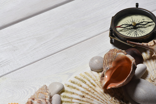 Vintage compass, seashells and pebble stones on the white wooden desk table close up background with copy space.