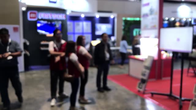 Visitors and representatives from companies that manufacture products observe modern industrial machinery for packaging automation on display in a hall. Intentional blurs