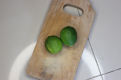Two yellowish-green organic limes are placed on a brown cutting board, which the seller gives free of charge if you buy vegetables in large quantities.