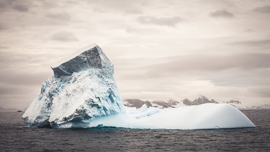 Dark Antarctica, Iceberg floating on the Antarctic Sound Ocean under dramatic dark overcast cloudscape. Antarctica Mountain Range in the background. Antarctica Ocean - Antarctica Sound, Antarctica.