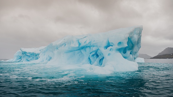 Antarctica Large Blue Glacier Iceberg - Natural Ice Sculpture - floating on the Antarctic Ocean under overcast cloudscape. Panorama Shot. Antarctica Ocean - Antarctica Sound, Antarctica.