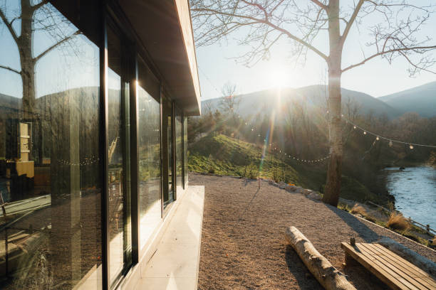 Photo of a wooden cabin house on riverbank, and its sliding glass door that lets the nature get in