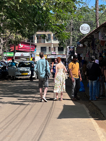 Palolem Beach, Goa, India - January, 10 2024: Stock photo showing close-up view of a group of tourists and locals passing by a row of beach gift shop kiosks selling holiday related products including summer clothing to tourists vacationing at Palolem Beach, Goa, India.