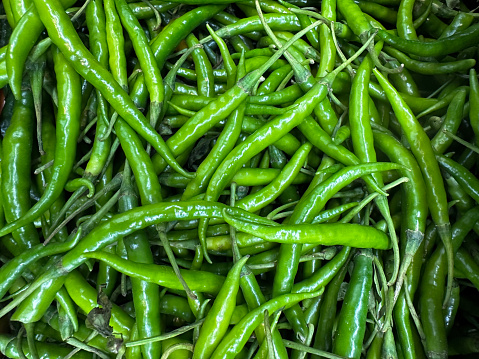 Stock photo showing close-up, elevated view of a pile of green chilli peppers (Capsicum) being sold in the fruit and vegetable aisle of a supermarket.