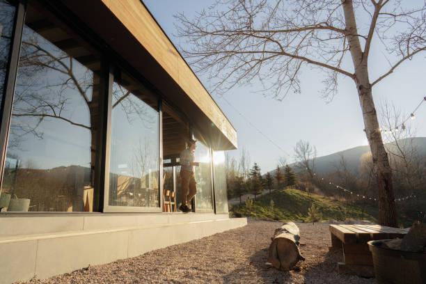 Photo of a wooden cabin house on riverbank, and its sliding glass door that lets the nature get in