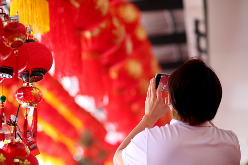 An Asian man is using smartphone taking photos of Chinese New Year decorations and red lanterns.