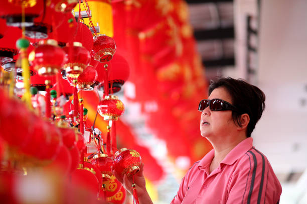 An Asian woman (wearing sunglasses protection from UVA/UVB after cataract surgery) is shopping for Chinese New Year red decorations and lanterns.