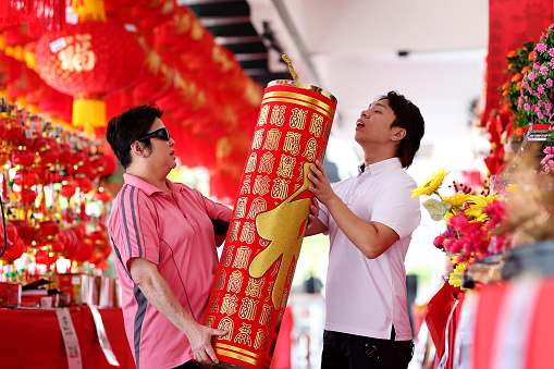 An Asian woman (wearing sunglasses protection from UVA/UVB after cataract surgery) and a man is taking a closer look on oversized decorative firecracker