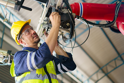 Professional caucasian white ethnicity male technician operating the heavy duty machine in the lathing factory. Technician in safety and helmet suit controlling a machine in factory.