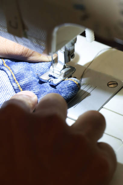 Stock photo of Indian man holding denim fabric and use sewing machine to stitch jeans to make alterations for a better fit.
