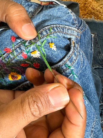 Stock photo showing close-up view of a pair of blue denim jeans sporting a customised design of embroidered flowers and leaves.
