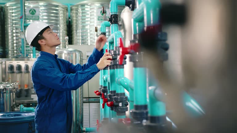 Maintenance engineer Worker in a hard hat adjusting valves and examining  pressure gauge on industrial piping in a water treatment facility. water bottling