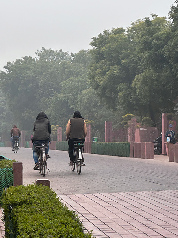 Agra, Uttar Pradesh, India - January 04, 2024: Stock photo showing hazy morning view of tourists cycling in the complex and formal gardens of the Taj Mahal.