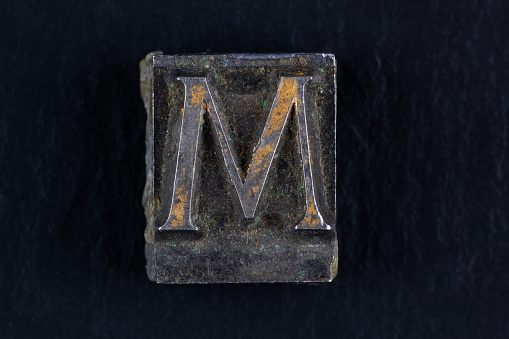 Antique vintage movable type alphabet letter M on black background.