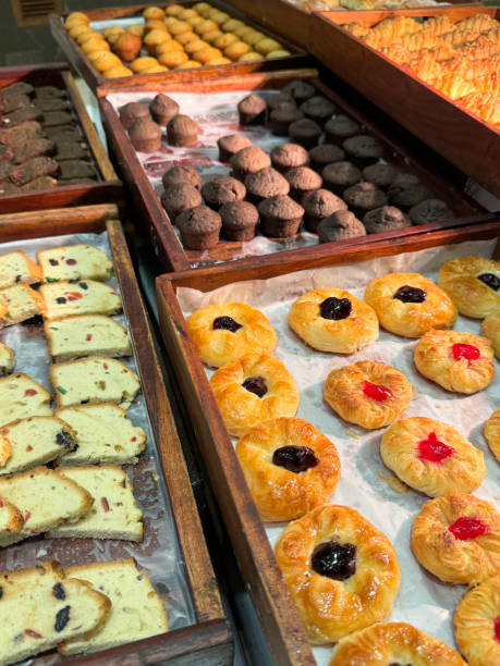 Close-up image of freshly baked breakfast pastries, croissants and cakes at hotel restaurant buffet, rows of sweet treats stacked on wooden tray lined with greaseproof parchment paper, elevated view, focus on foreground