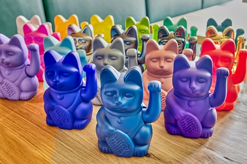 Charming assortment of Japanese maneki neko cats, featuring various colors, displayed on a wooden table, evoking luck and good fortune in japanese tradition and culture.