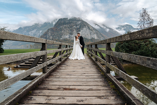 Kissing bride and groom embracing and posing on a bridge background of lake and mountains. Loving couple together. Stock photo