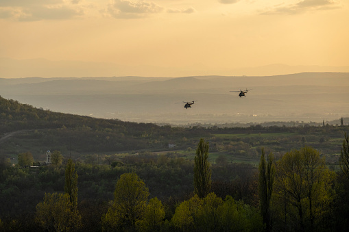 Two helicopters fly over the fields and forests.