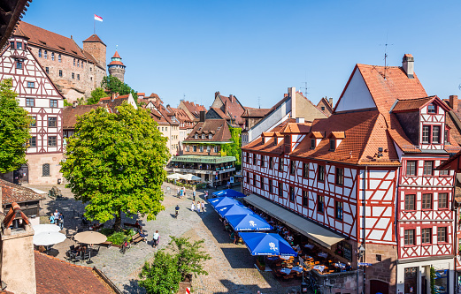 Nuremberg, Germany - August 23, 2023: High angle view of the Tiergärtnertor square lined with medieval half-timbered buildings and sidewalk cafes, overlooked by the towers of the castle.